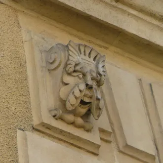 Sculpture ornementale en pierre représentant une tête grotesque avec des cheveux bouclés, intégrée dans l'architecture d'une façade bordelaise ancienne.