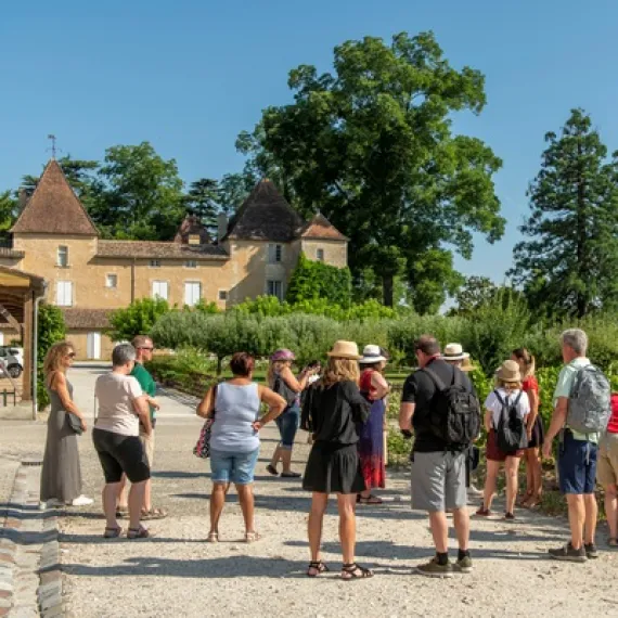 Tour group standing in front of a historic château featuring distinctive pointed towers and ochre-colored stonework, typical of Bordeaux architecture.