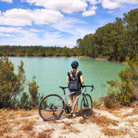 Cycliste à vélo devant un lac aux eaux turquoise au cœur des paysages naturels de Gironde.