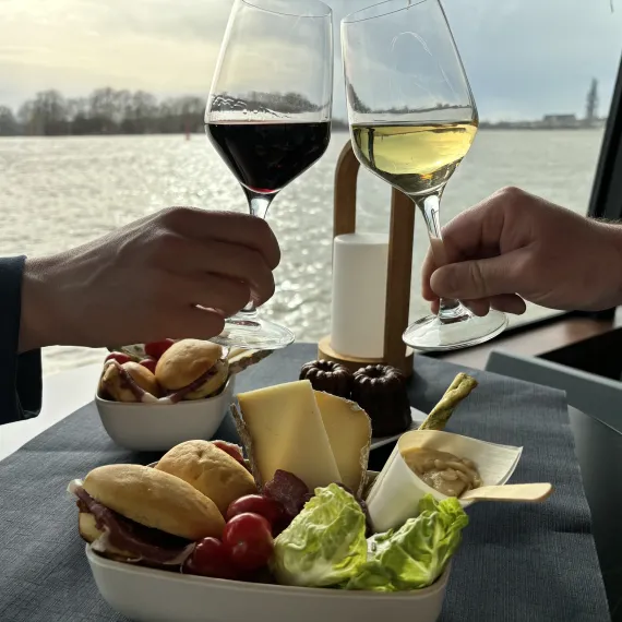 Participant dégustant un verre de vin blanc et un verre de vin rouge accompagnés d'une planches d'assortiments lors d'une croisière à Bordeaux.