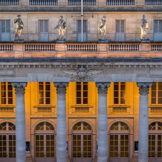 Détail de la façade du Grand Théâtre de Bordeaux au crépuscule, mettant en valeur ses colonnes corinthiennes, ses statues monumentales et son architecture néoclassique du XVIIIᵉ siècle.