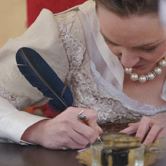 Femme en costume historique écrivant à la plume lors d'une animation dans un château.