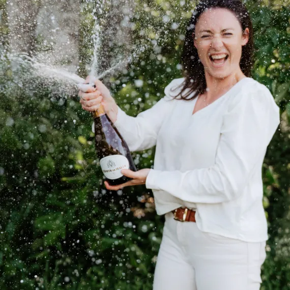Femme ouvrant une bouteille de vin effervescent lors d'un pique-nique en plein air dans un cadre verdoyant.
