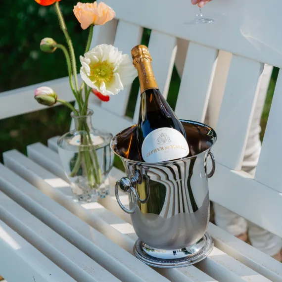Visuel illustrant une bouteille de vin blanc en plein air sur un banc accompagnée de fleurs champêtres