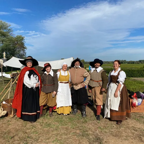 Groupe de personnes en costumes historiques dans les vignes, devant un campement d'époque.