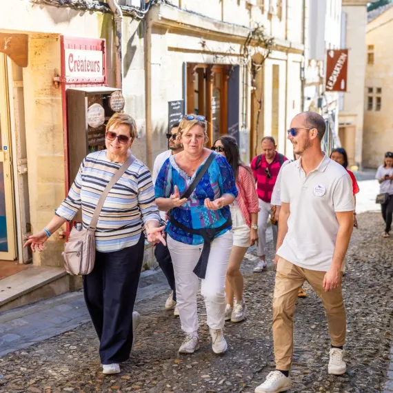 Guide touristique accompagnant un groupe de visiteurs dans les ruelles pavées du village médiéval de Saint-Émilion.