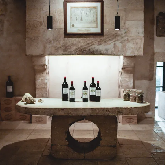 Salle de dégustation en pierre avec cinq bouteilles de vin sur une table centrale.