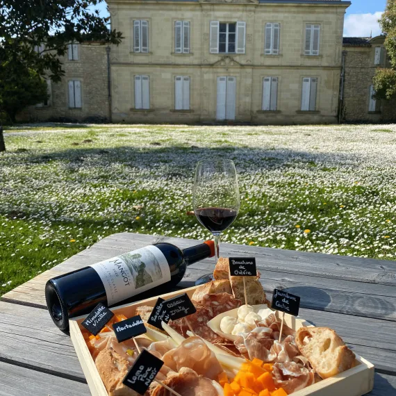 Planche de charcuterie et fromages avec bouteille et verre de vin rouge Château Mangot, devant la façade du château, Saint-Émilion.