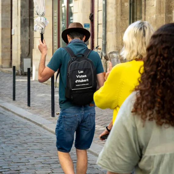 Un guide portant un sac à dos conduit un groupe de visiteurs dans une rue pavée de Bordeaux.