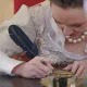 Femme en costume historique écrivant à la plume lors d'une animation dans un château.