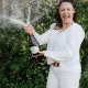 Femme ouvrant une bouteille de vin effervescent lors d'un pique-nique en plein air dans un cadre verdoyant.