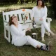 Deux femme dégustant une bouteille de vin effervescent au pied d'un banc dans un cadre verdoyant.