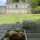 Verres à vin et planche apéritive dressés sur une table en bois face au Château Mangot, dans le parc arboré.